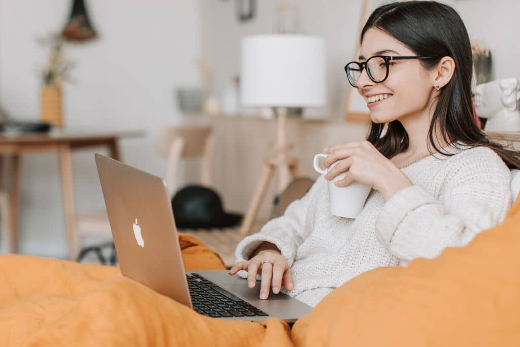 Chica sonriente con portátil y café tras escribir una descripción atractiva de su piso para venderlo